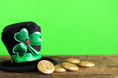 Black leprechaun hat and gold coins on wooden table against green background, space for text. St. Patrick's Day celebration