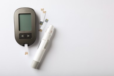 Photo of Digital glucometer, lancet pen and test strips on white background, flat lay with space for text. Diabetes control