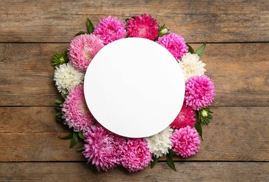 Flat lay composition with blank card and beautiful asters on wooden table, space for text. Autumn flowers
