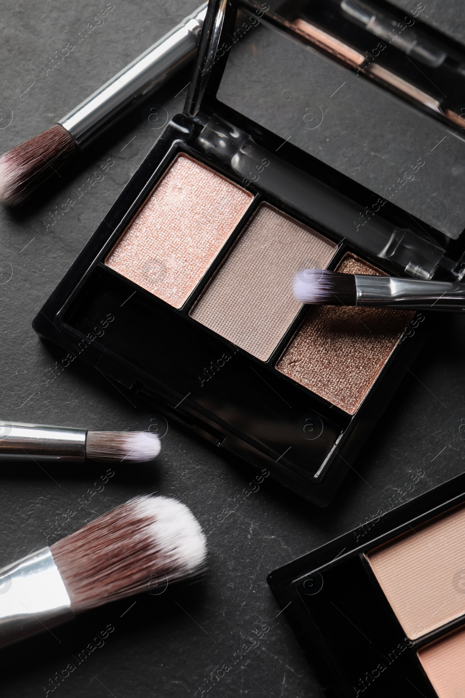 Photo of Beautiful eye shadow palettes and brushes on dark grey textured table, flat lay