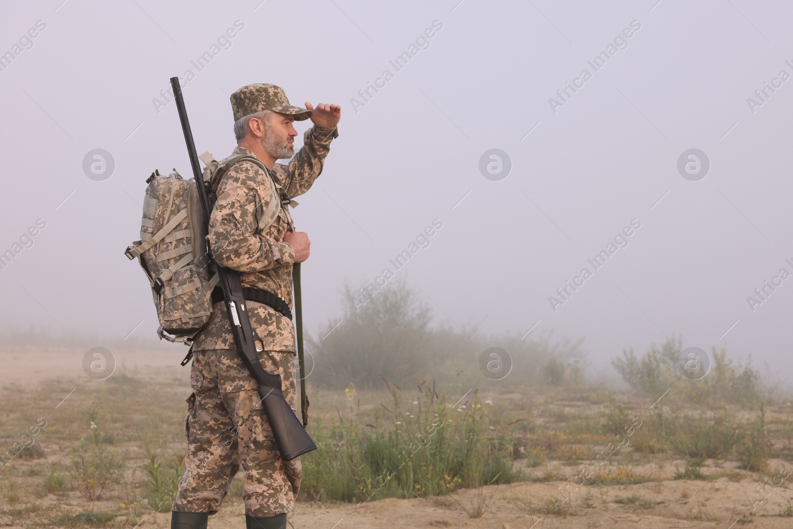 Photo of Man wearing camouflage with hunting rifle and backpack outdoors. Space for text