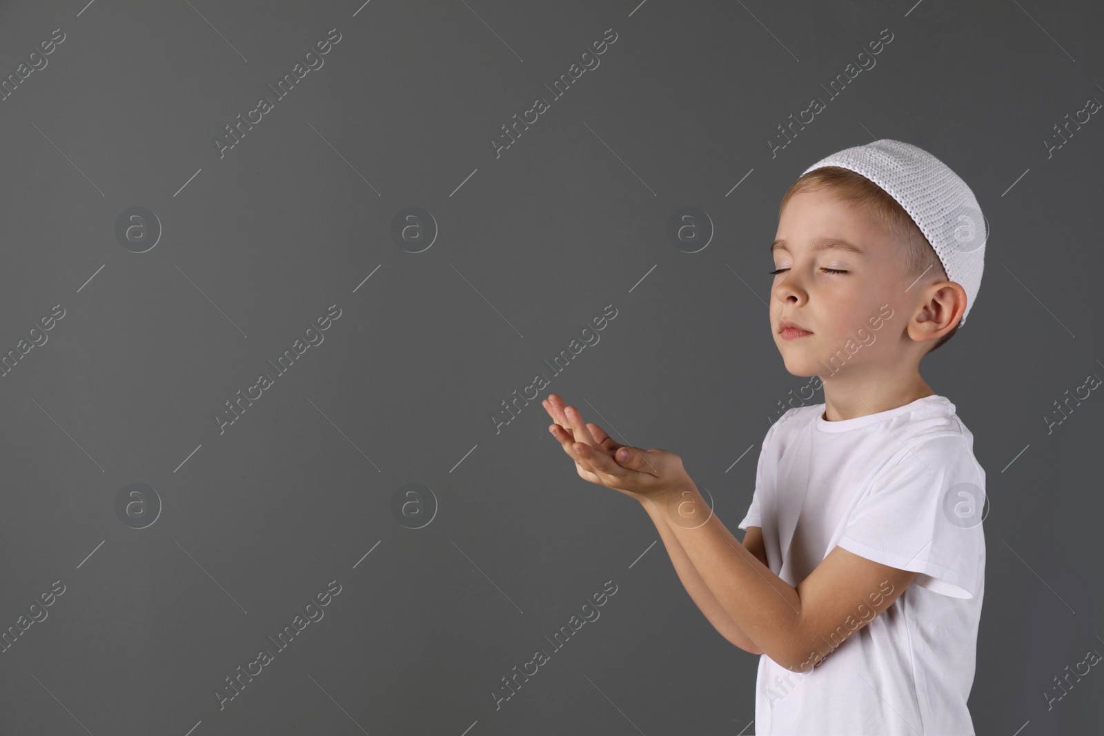 Photo of Little Muslim boy praying on gray background. Space for text
