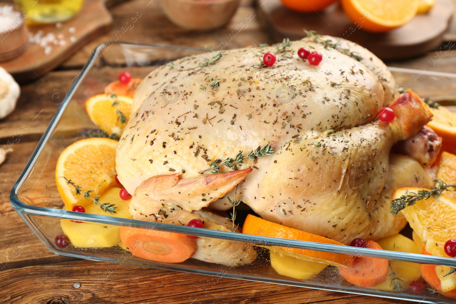 Photo of Raw chicken, orange slices and other ingredients in baking dish on wooden table