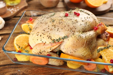 Raw chicken, orange slices and other ingredients in baking dish on wooden table