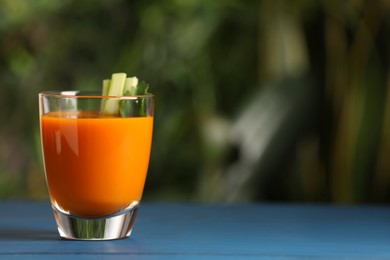 Glass with tasty carrot juice on blue wooden table outdoors. Space for text
