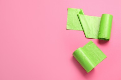 Rolls of green garbage bags on pink background, flat lay. Space for text