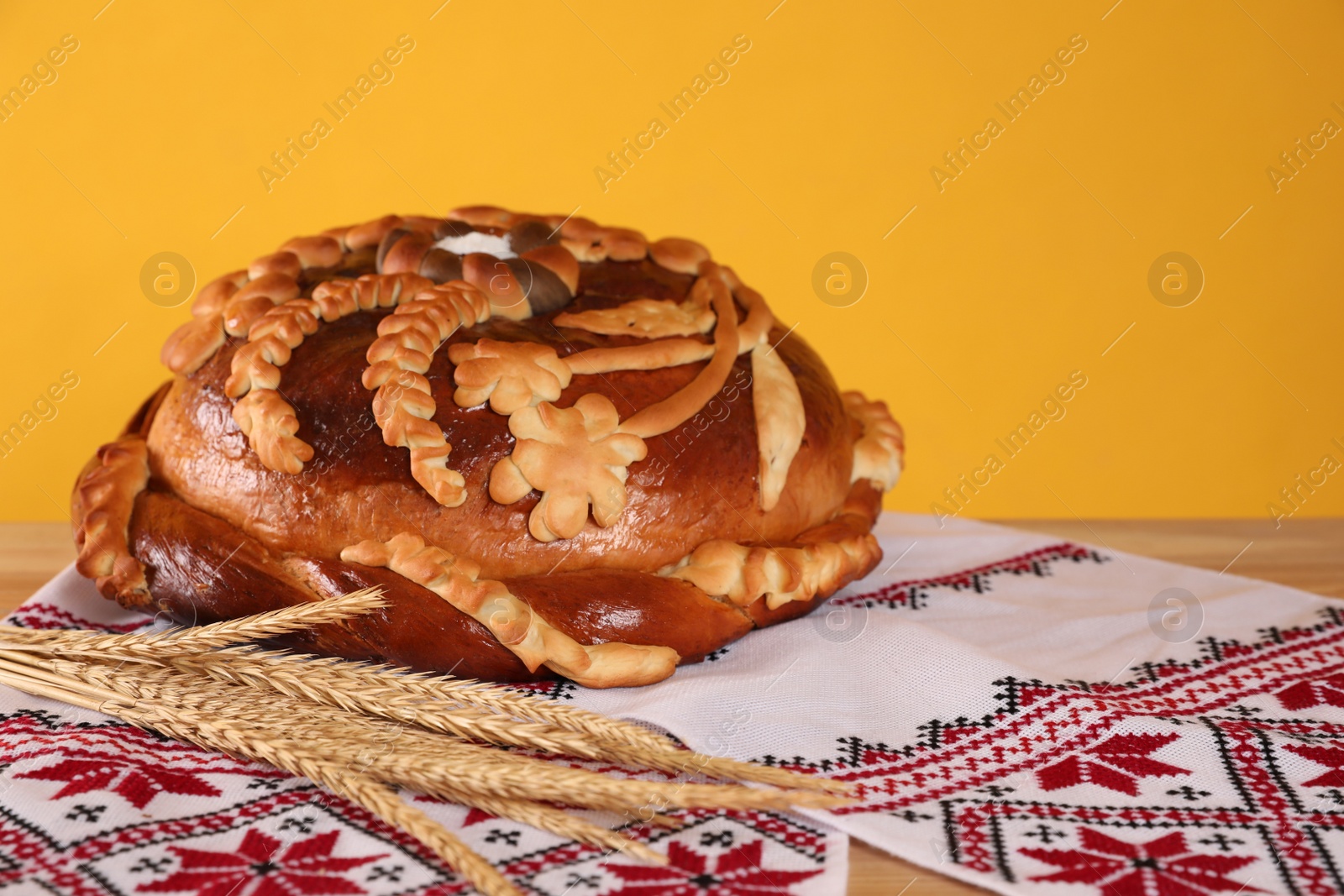 Photo of Rushnyk with korovai, wheat spikes on yellow background. Ukrainian bread and salt welcoming tradition