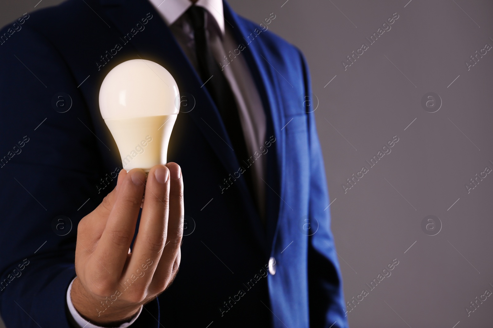 Photo of Businessman holding lamp bulb against gray background, closeup. Space for text