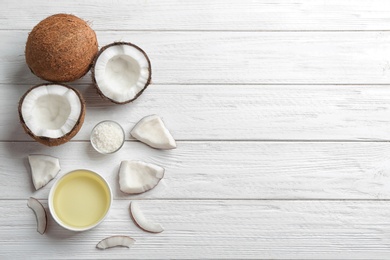 Photo of Bowl of natural organic oil and coconuts on white wooden background, flat lay. Space for text