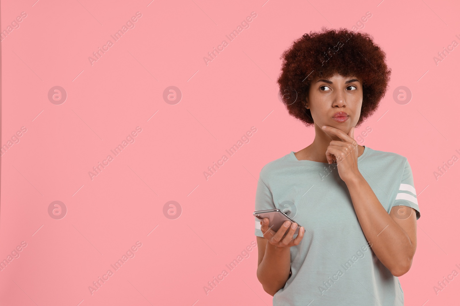 Photo of Thoughtful young woman with smartphone on pink background. Space for text