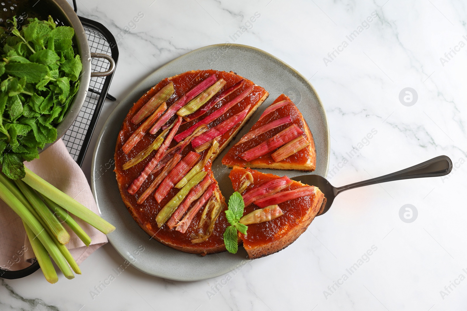 Photo of Freshly baked rhubarb pie, stalks and cake server on white marble table, flat lay