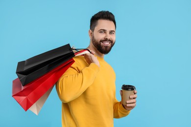 Photo of Smiling man with paper shopping bags and takeaway coffee on light blue background