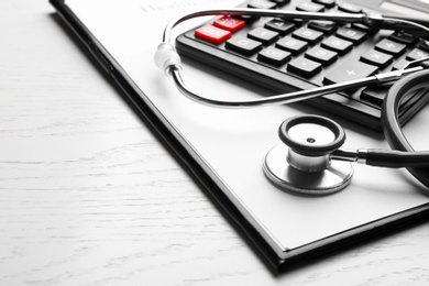 Photo of Stethoscope with clipboard and calculator on white wooden table, closeup. Medical insurance concept