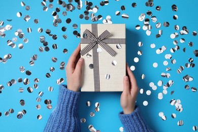 Woman with Christmas gift and confetti on light blue background, top view