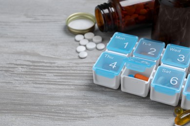 Weekly pill box with medicaments on wooden table, closeup. Space for text
