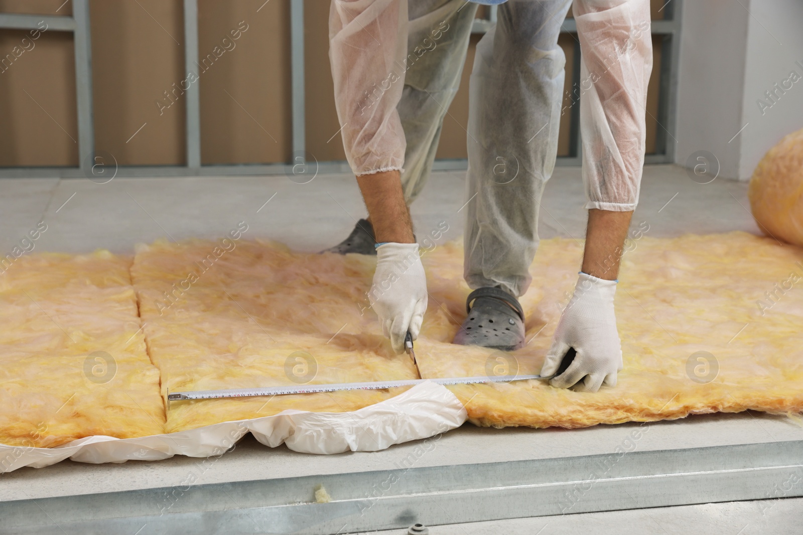 Photo of Worker measuring and cutting insulation material indoors, closeup. Space for text