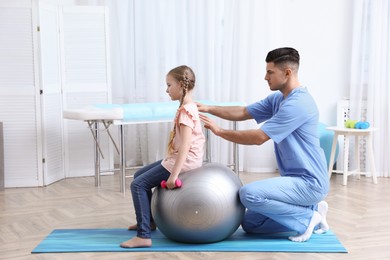 Photo of Orthopedist helping child to do exercise with dumbbell in clinic. Scoliosis treatment
