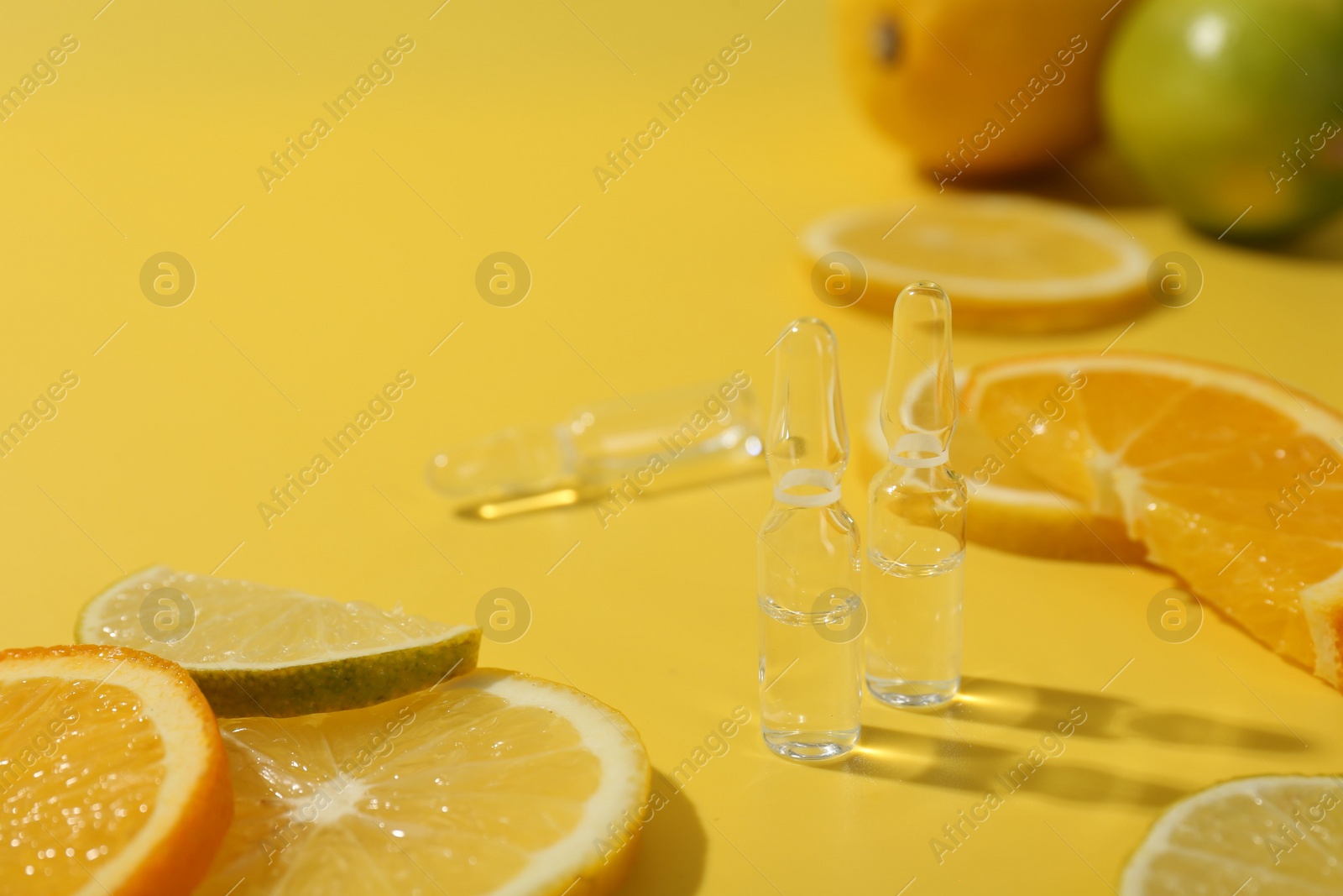 Photo of Skincare ampoules with vitamin C and citrus slices on yellow background, closeup. Space for text