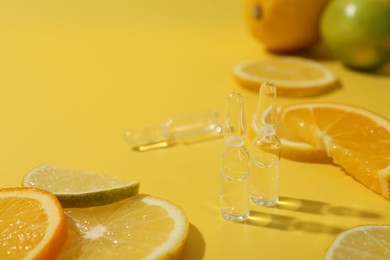 Skincare ampoules with vitamin C and citrus slices on yellow background, closeup. Space for text