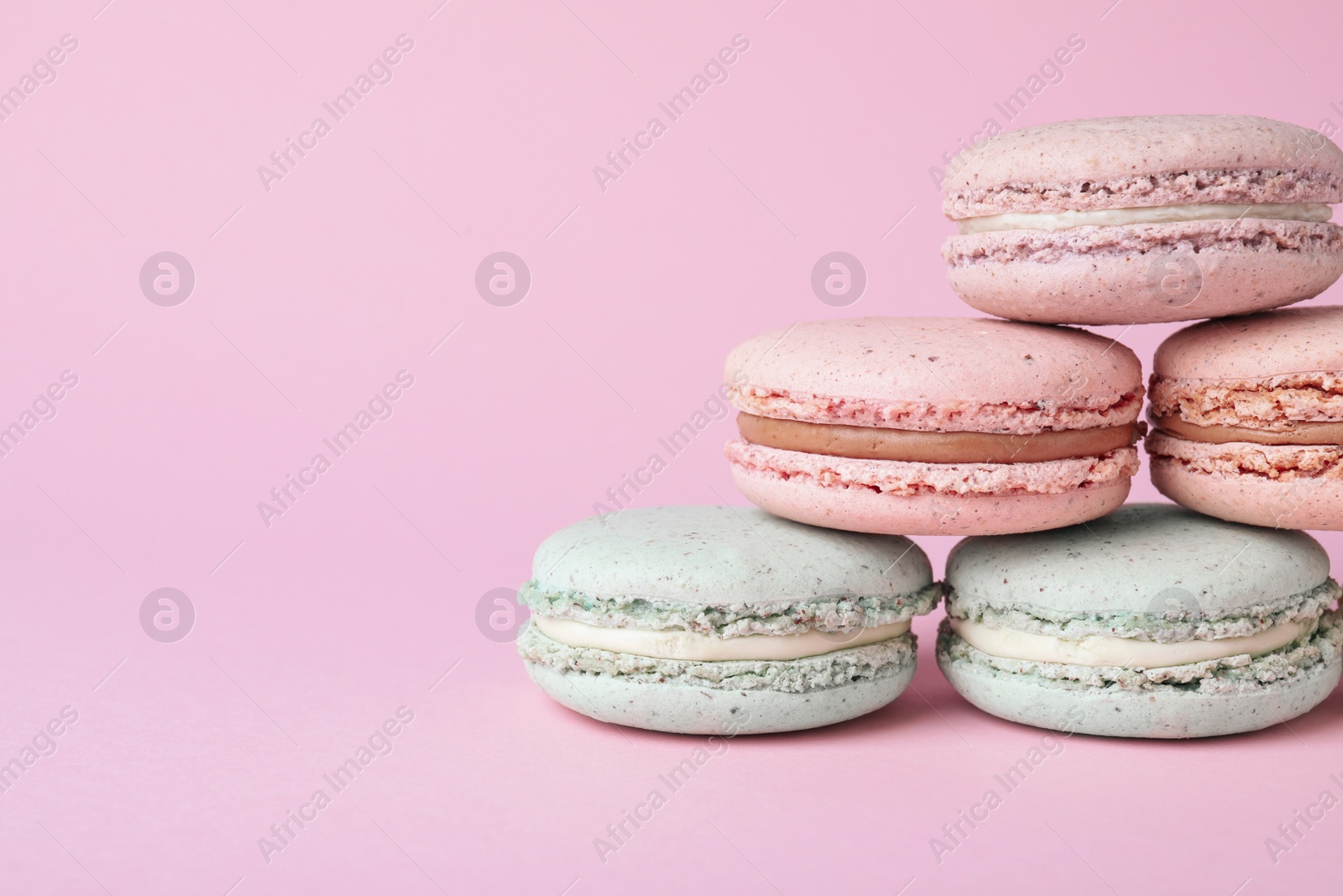 Photo of Pile of delicious colorful macarons on pink background, closeup. Space for text