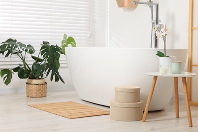 Photo of Stylish bathroom interior with bath tub, houseplants and bamboo mat