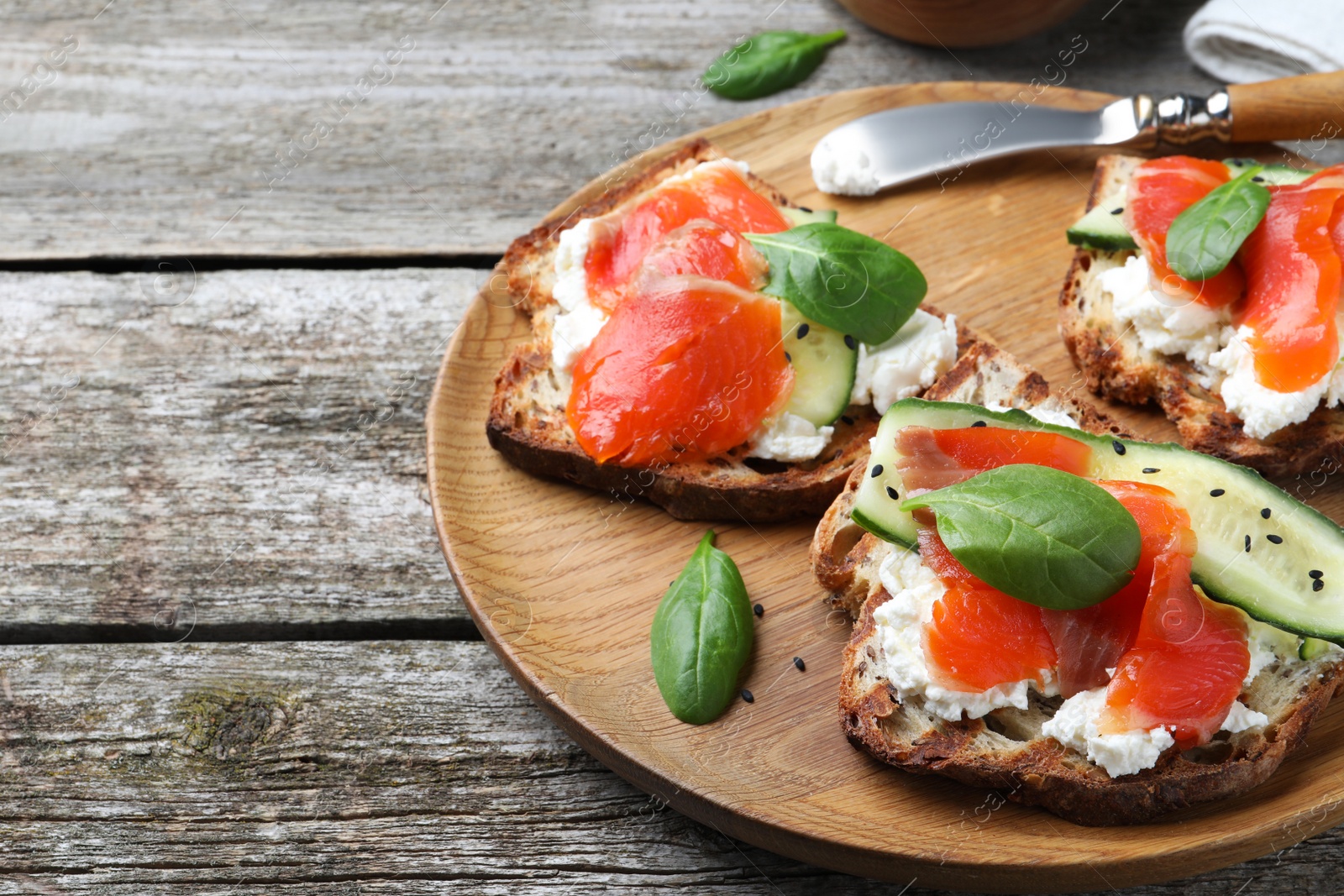 Photo of Delicious sandwiches with cream cheese, salmon, cucumber and spinach on wooden table. Space for text