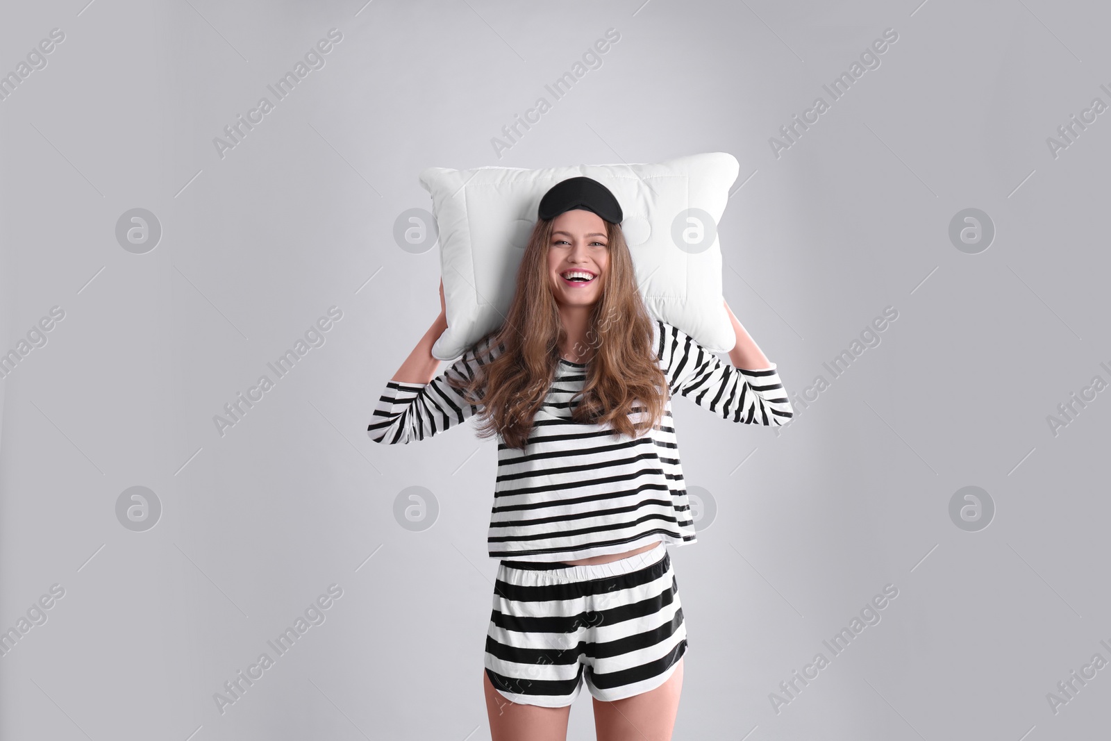 Photo of Happy woman in pajamas with pillow on gray background