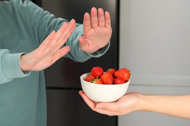 Photo of Woman suffering from food allergies refusing offered strawberries by her friend at home, closeup