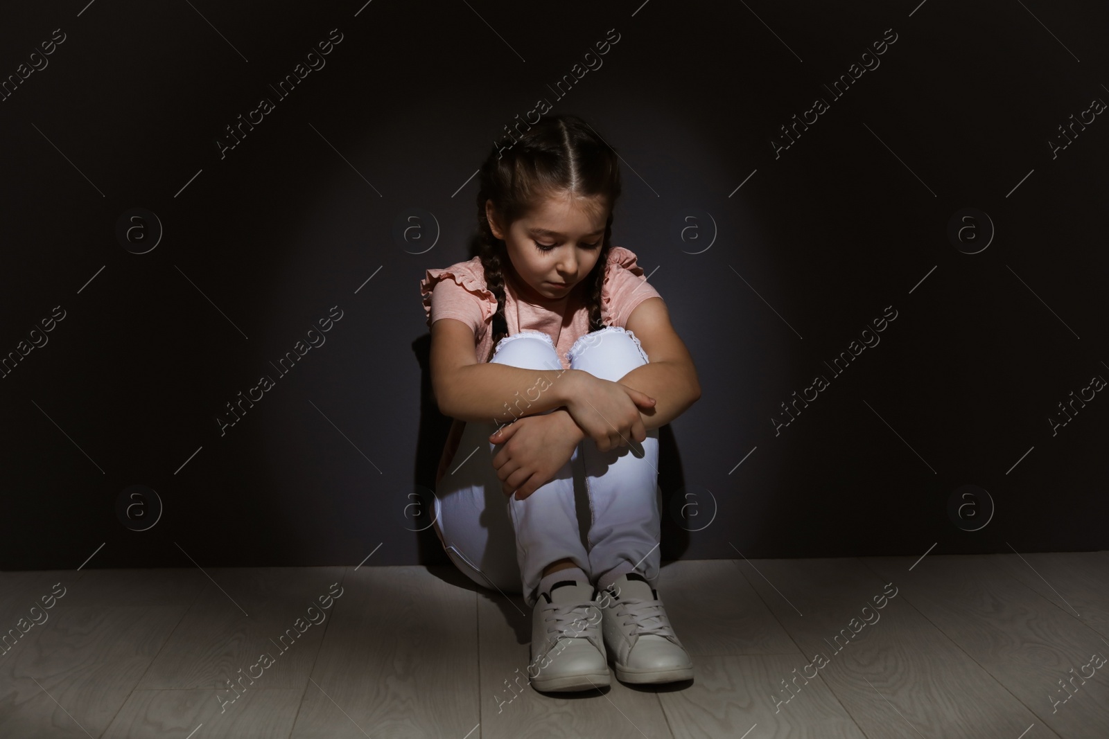 Photo of Depressed little girl sitting on floor indoors. Time to visit child psychologist