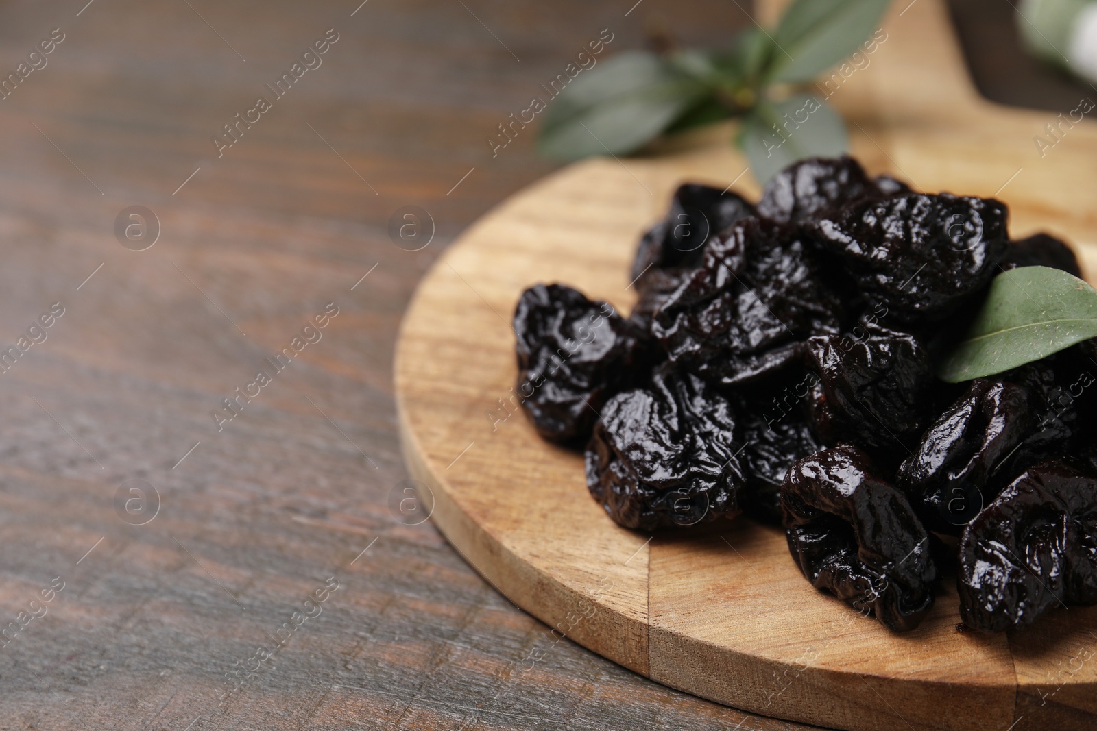 Photo of Tasty dried prunes and green leaf on wooden table, closeup. Space for text