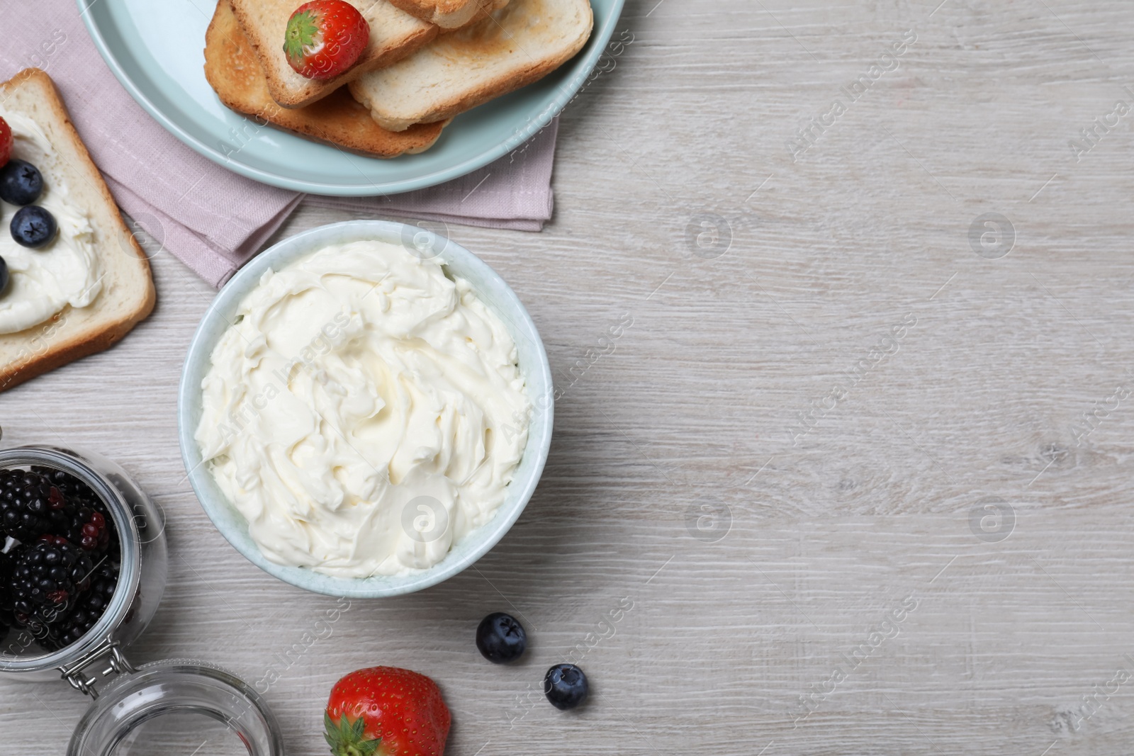 Photo of Tasty cream cheese, toasted bread and fresh berries on white wooden table, flat lay. Space for text