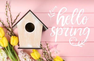 Hello Spring. Flat lay composition with bird house and flowers on pink wooden background 