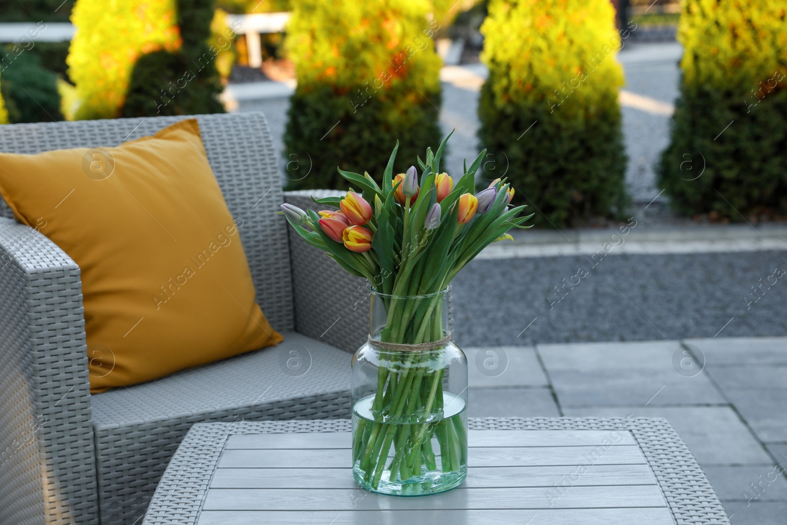 Photo of Beautiful bouquet of colorful tulips on rattan garden table outdoors