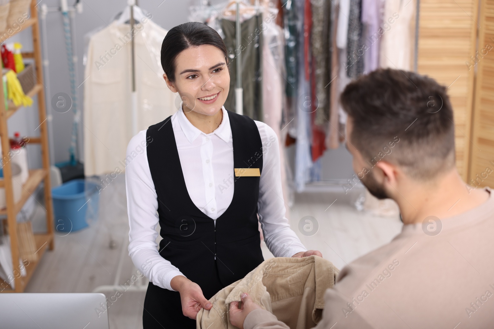 Photo of Dry-cleaning service. Happy worker receiving coat from client indoors