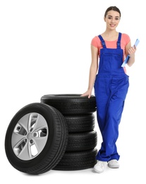 Female mechanic in uniform with car tires and clipboard on white background