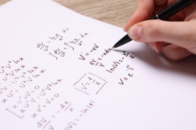 Photo of Student writing different mathematical formulas on paper, closeup