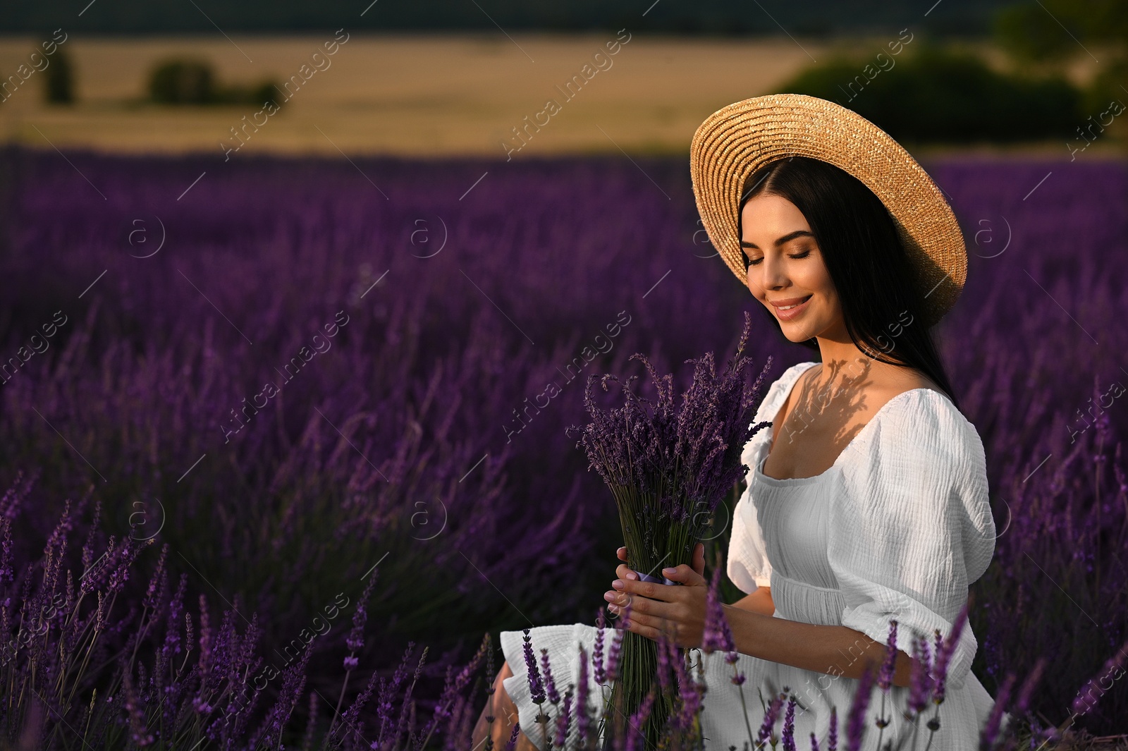 Photo of Beautiful young woman with bouquet sitting in lavender field