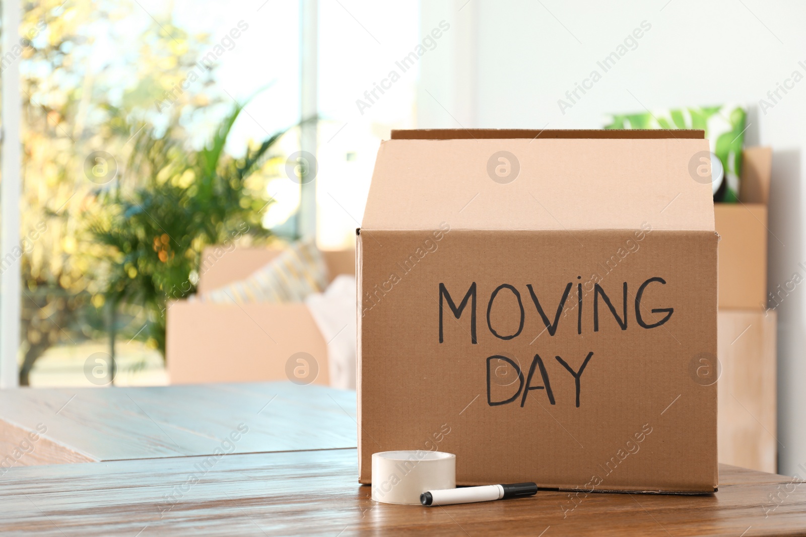 Photo of Cardboard box with words MOVING DAY and packaging items on wooden table