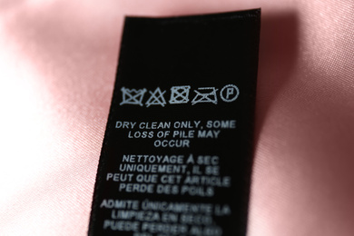 Photo of Clothing label with care symbols on pink silk shirt, closeup view