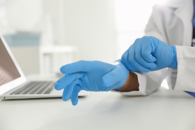 Photo of Doctor putting on medical gloves at table in office, closeup