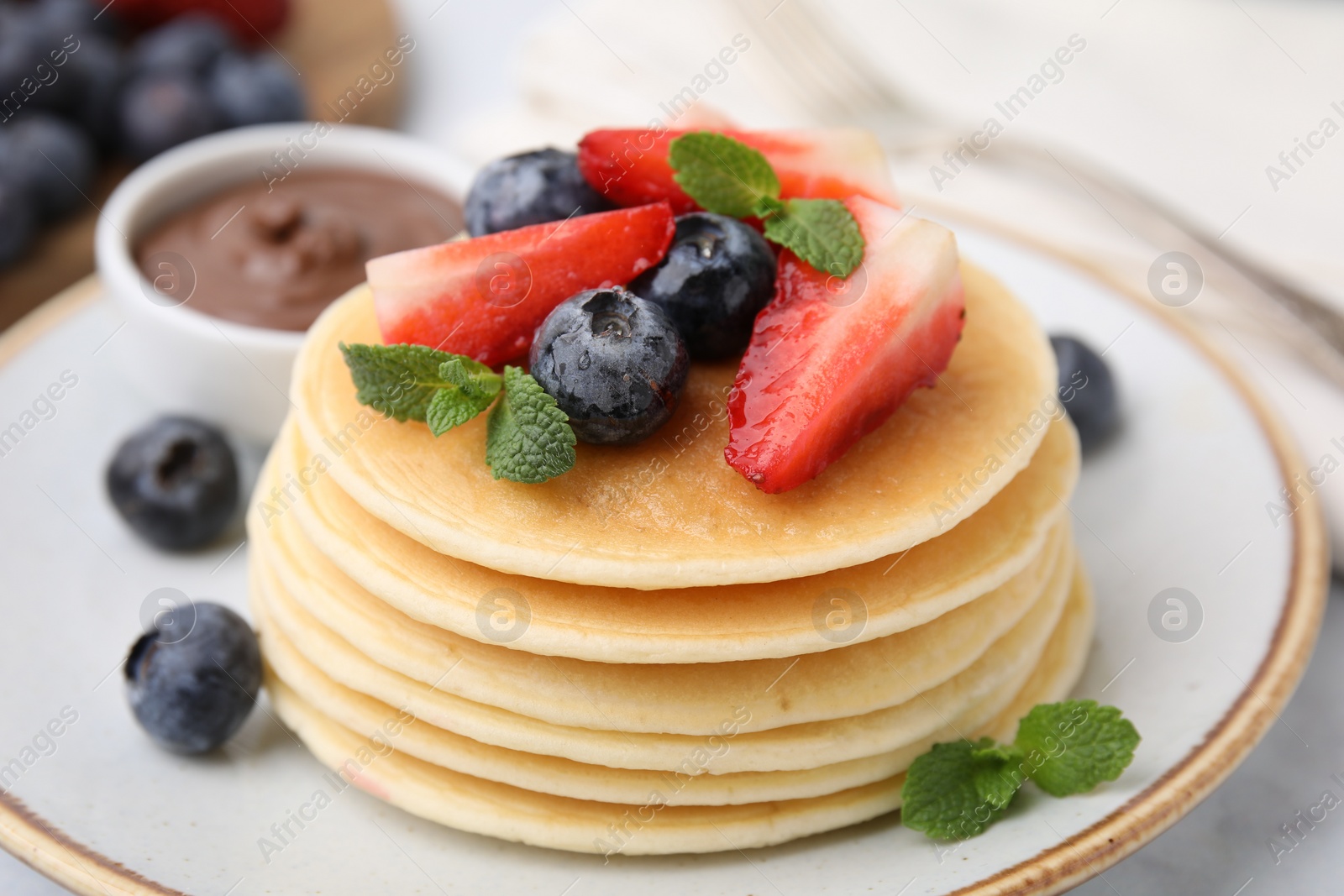 Photo of Delicious pancakes with strawberries, blueberries and chocolate sauce on table, closeup