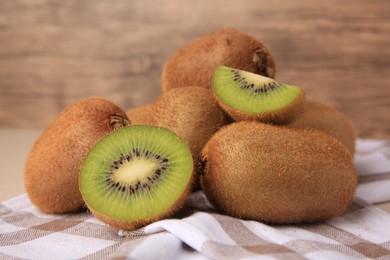 Photo of Heap of whole and cut fresh kiwis on checkered tablecloth, closeup