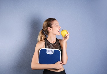 Photo of Young beautiful woman with scales and apple on color background. Weight loss motivation