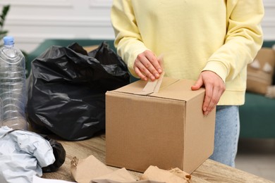 Photo of Woman with cardboard box separating garbage in room, closeup