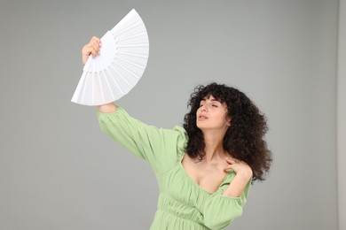 Photo of Woman with hand fan suffering from heat on light grey background