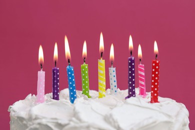 Delicious cake with cream and burning candles on pink background, closeup