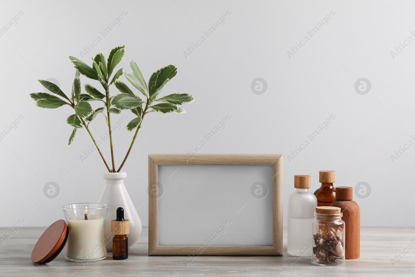 Photo of Blank photo frame, different bottles and decor elements on wooden table