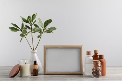 Blank photo frame, different bottles and decor elements on wooden table