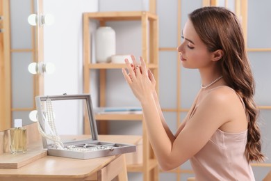 Photo of Young woman trying on elegant ring with pearls indoors