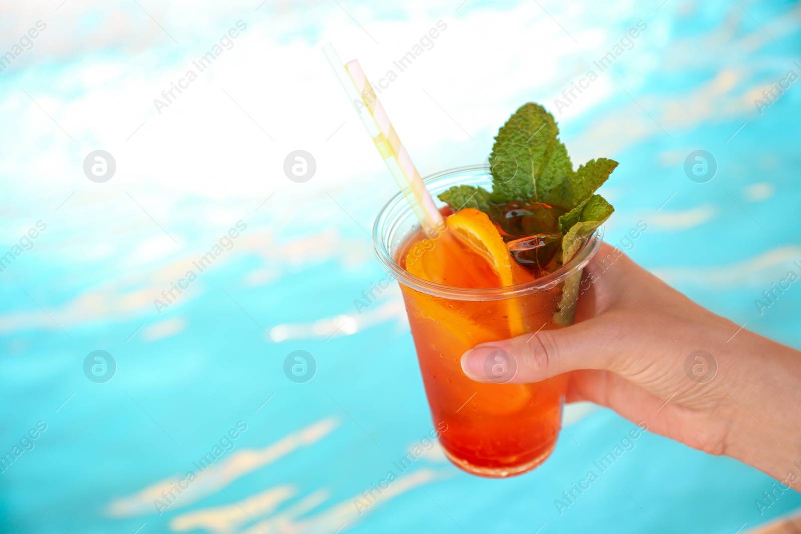 Photo of Woman with glass of refreshing drink near swimming pool, closeup. Space for text